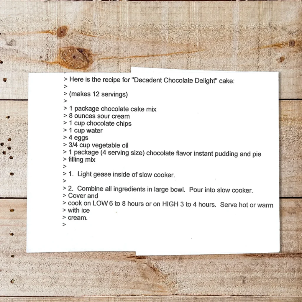 A printed recipe card on a wooden surface featuring the "Decadent Chocolate Delight" cake recipe. The text lists ingredients like chocolate cake mix, sour cream, chocolate chips, and eggs, followed by step-by-step instructions for making the cake in a slow cooker.